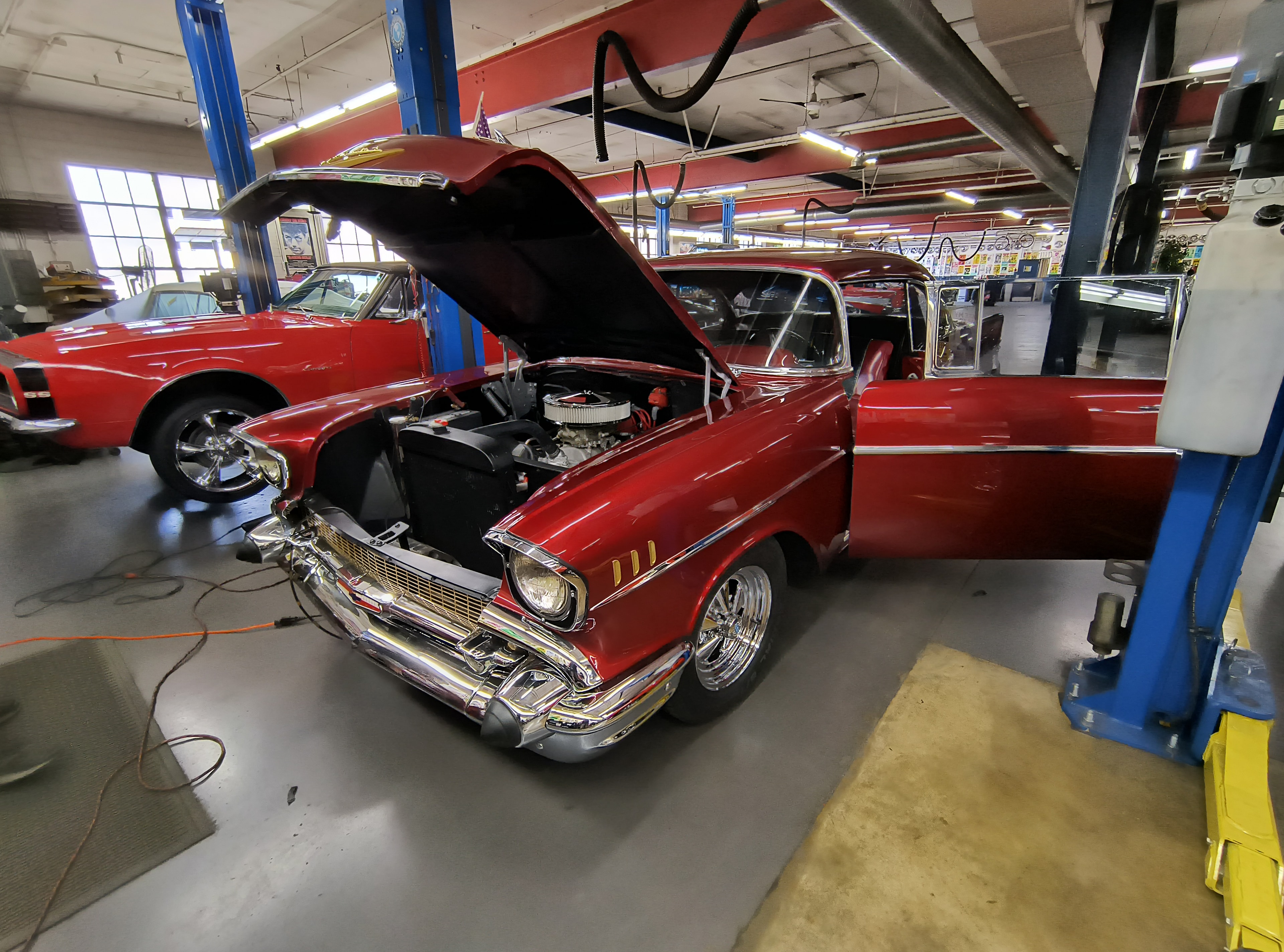 Red 1957 Chevrolet Bel Air with hood open on inspection lift in shop, Iowa pre-purchase inspection