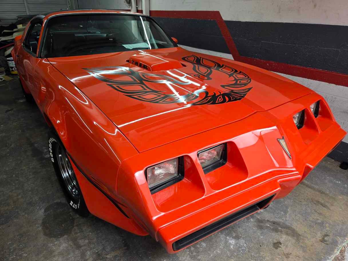 Orange Pontiac Firebird Trans Am with hood bird graphic, garage setting